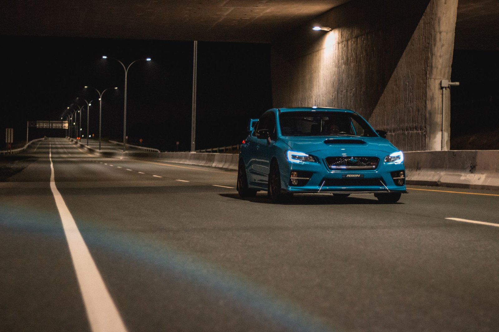 A modern car driving on a winding road with bright LED headlights at twilight.