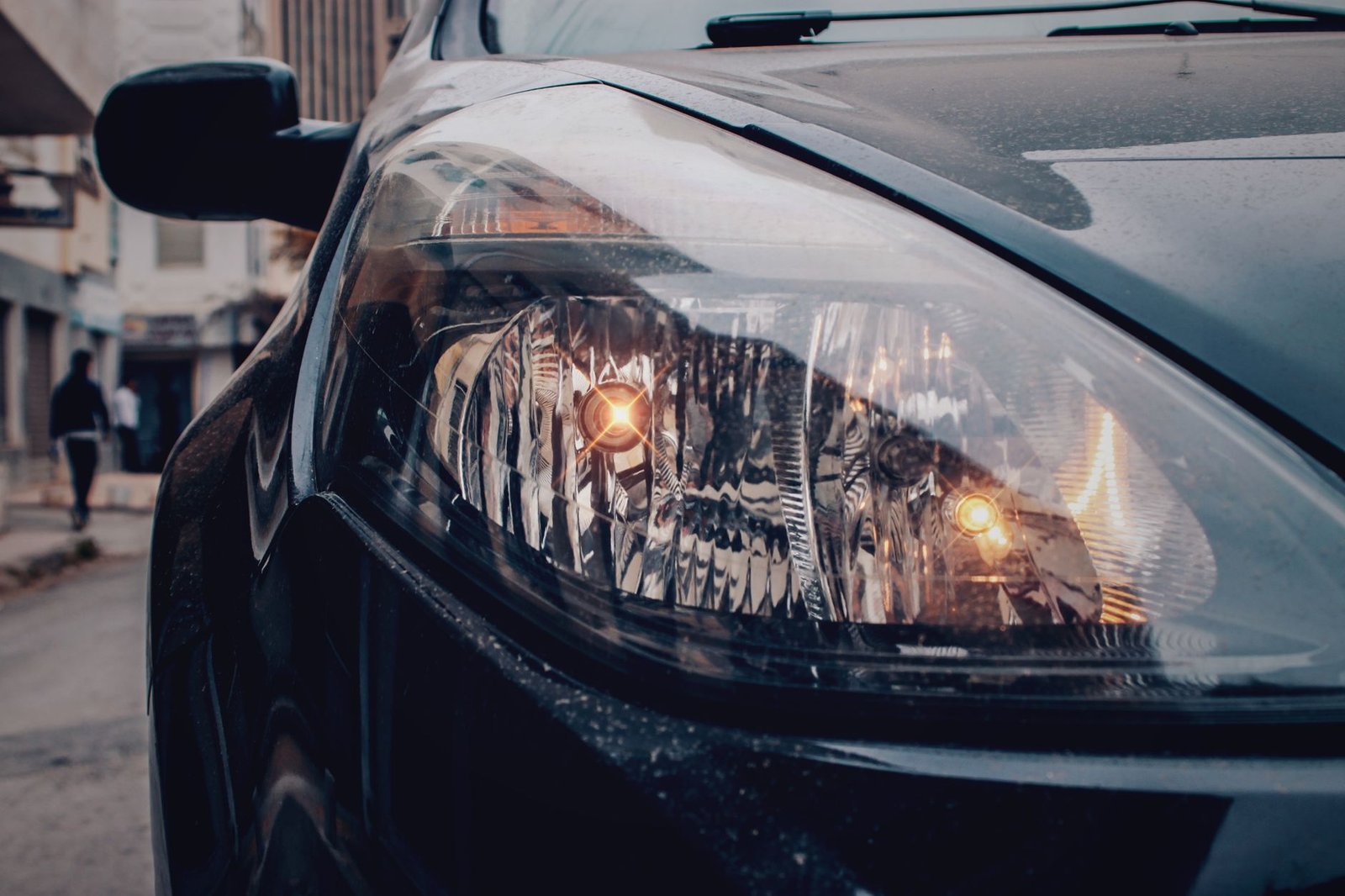 A modern car headlight with a bright projector lens emitting a clean white beam.